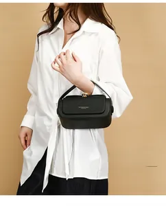Detail of black leather crossbody bag with gold metal clasp on white shirt background