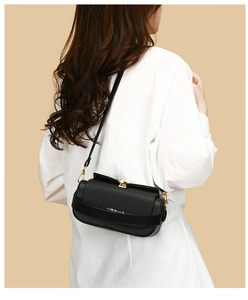 Detail of black leather cylindrical shoulder bag with gold clasp shown on a model