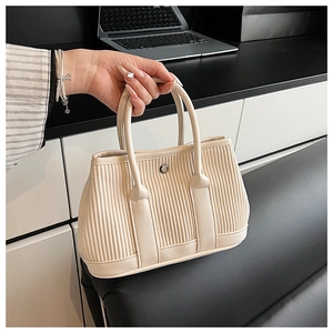 Detail of beige pleated faux leather handbag showing vertical texture and magnetic buckle
