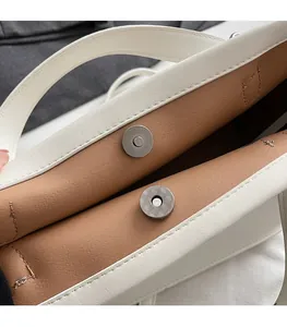 Close-up of metal magnetic snap closure on white handbag with brown suede lining