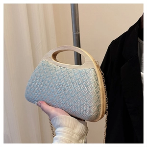 Detail of blue and beige woven straw bag featuring a trapezoidal wooden handle and gold chain