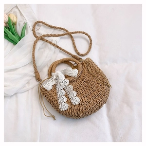 Detail of straw woven bag with white lace bow and drawstring closure on fabric