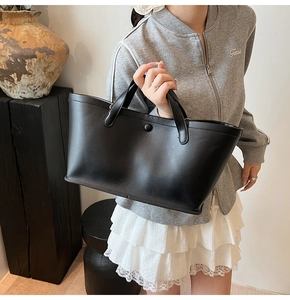 Minimalist black matte leather tote bag styled with white lace dress in aesthetic setting