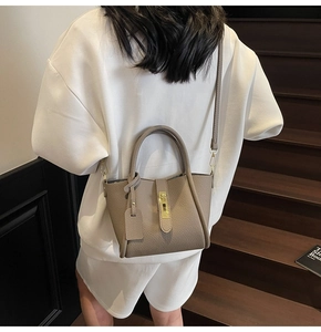Detailed view of taupe leather handbag featuring gold twist lock and fine grain texture