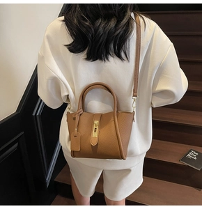 Detail of a brown leather shoulder bag with gold hardware worn by a model on a staircase