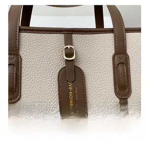 Close-up of beige litchi grain tote bag with brown leather handles and gold buckle hardware