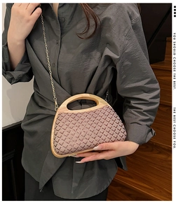 Detail of a straw woven handbag with wooden handle and gold chain strap in a lifestyle setting