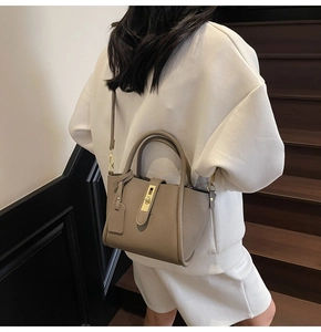 Detail of grey lychee leather crossbody bucket bag with gold clasp shown on a model