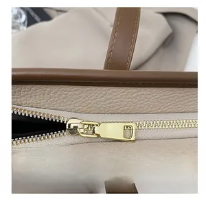 Detail of smooth gold metal zipper and beige lychee pattern leather on tote bag