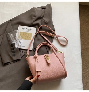 Detail of pink lychee leather handbag featuring a golden turn-lock and adjustable strap