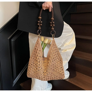 Detail of hollow woven straw handbag with dark beaded handle and diamond texture