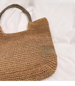Detail of woven straw tote bag featuring contrast black and white striped rope handles