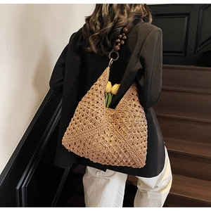 Detail of woven straw tote bag with dark wooden bead handles and hollow-out texture