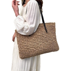 Grand sac cabas en paille tressée marron clair avec anses en cuir noir sur fond blanc