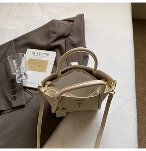 Top view of beige lychee pattern handbag with gold hardware on a white bed setting