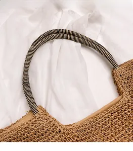 Detail of hand-woven straw bag featuring striped cylindrical handle on white fabric