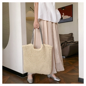 Detail of hand-woven beige straw tote bag with striped straps in minimalist home setting