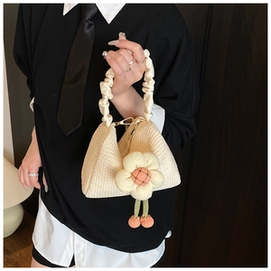 Detail of off-white straw woven handbag featuring floral charm and ruffled handle
