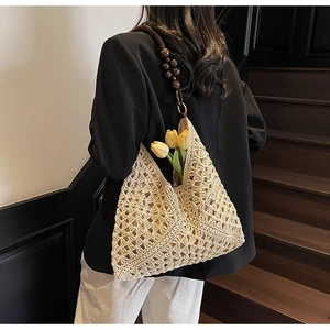 Detail of hand-woven straw hobo bag with hollow crochet pattern and wooden bead strap