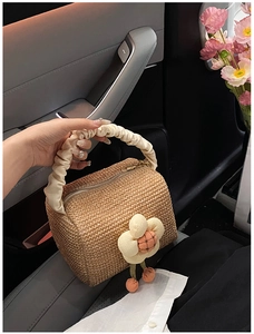 Detail of straw handbag featuring cream pleated handles and decorative large fabric flower