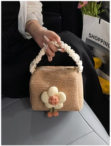 Detail of straw handbag featuring large floral applique and white pleated handles