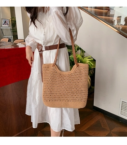 Close-up of woven hollow knit tote with brown leather handles and metal rivet details