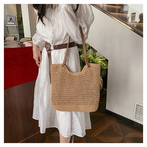 Close-up of beige woven tote bag with brown leather straps held by a model in a dress