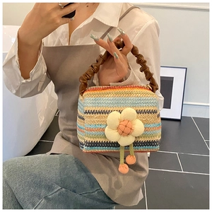 Detail of rainbow straw handbag featuring 3D white flower and plush pompom charms