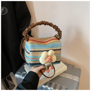 Detail of colorful striped straw handbag featuring a floral charm and brown leather handle