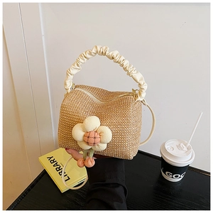 Detail of straw woven handbag featuring beige pleated handle and plush flower pendant