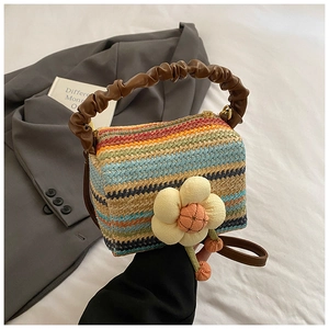 Detail view of colorful striped straw handbag with yellow flower and brown ruched handle