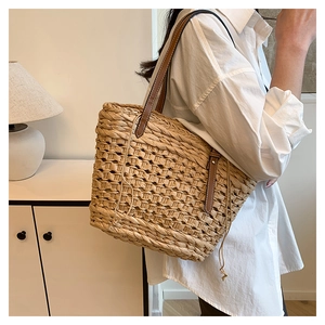 Gros plan du sac cabas en paille tressée avec bandoulière en cuir et rivets sur modèle