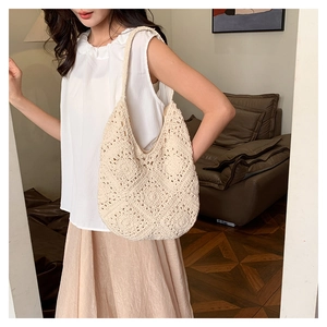 Close-up of cream woven crochet shoulder bag with hollow floral pattern on a sofa