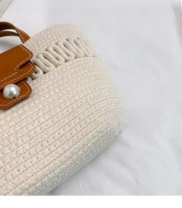 Close-up of beige woven bucket bag featuring brown leather trim and a large pearl ornament