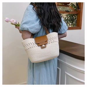 Detail of woven straw tote bag with pearl closure and brown leather straps