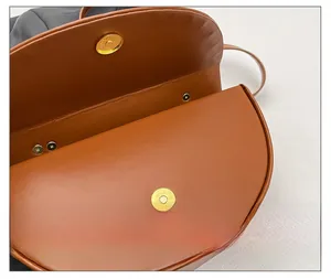 Detail of the golden magnetic buckle closure on a brown leather saddle handbag