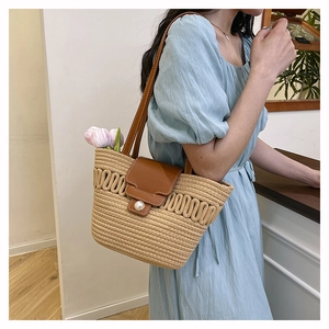 Detail of woven straw tote bag featuring brown leather trim and large pearl buckle closure
