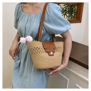Close-up of woven straw bucket bag featuring dark brown leather strap and pearl buckle detail