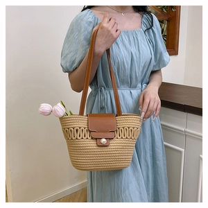 Detail of woven straw tote bag featuring a leather strap and a large pearl button closure