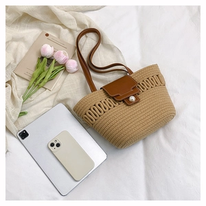 Detail of woven straw tote bag with brown leather strap and large pearl closure