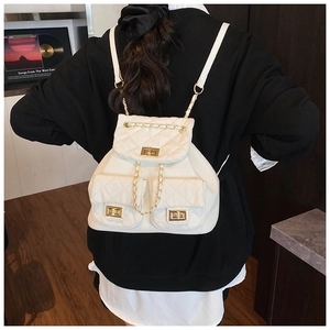 Back view of a quilted ivory backpack with golden chain straps on a black outfit