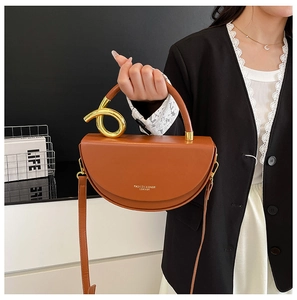Detail view of brown leather saddle bag with twisted gold ring and adjustable strap