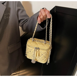 Detailed macro view of yellow quilted mini box bag featuring crystals and camellia pendant