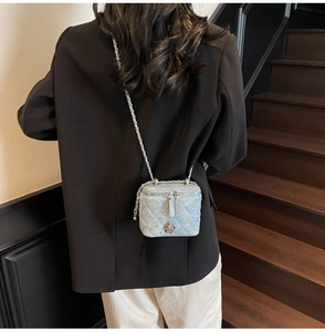 Detail of blue quilted denim mini box bag with metal camellia pendant and chain strap