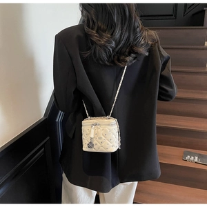 Detail of cream quilted mini bag with crystal studs and camellia charm on chain strap