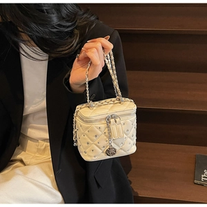 Close-up of quilted beige mini bag with rhinestone details and a silver camellia charm