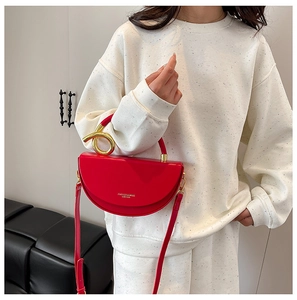 Detail of red saddle bag featuring a unique gold metal knot handle and adjustable strap