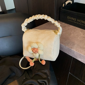 Chic beige straw beach bag with floral charm and pleated handle shown from a 45-degree angle