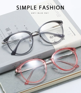 Detail of two stylish cat-eye anti blue light glasses in gray and pink frames on books