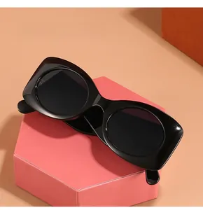 Detail view of oval sunglasses with thick black frames on a pink display stand